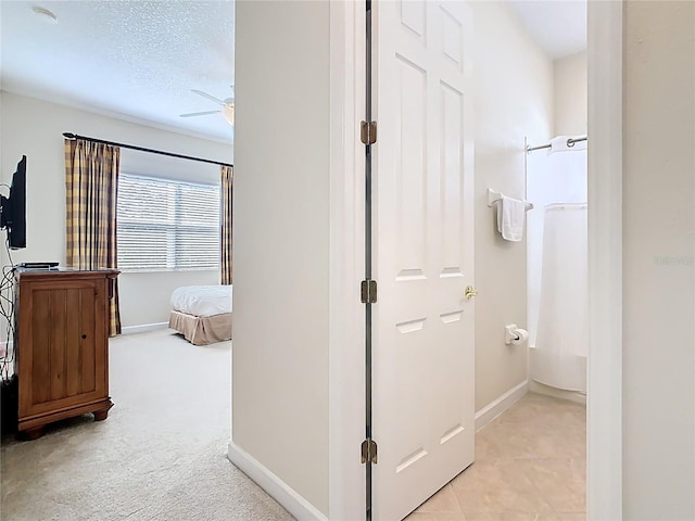 corridor featuring light carpet, a textured ceiling, and baseboards