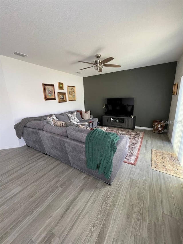 living room with visible vents, ceiling fan, a textured ceiling, wood finished floors, and baseboards