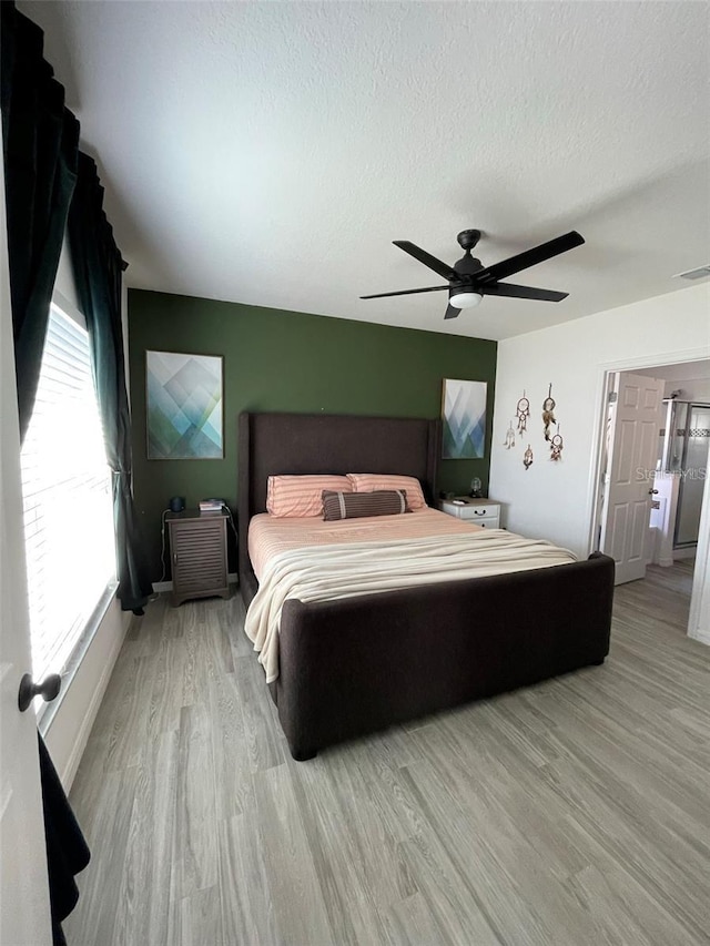 bedroom featuring light wood-type flooring, ceiling fan, visible vents, and a textured ceiling