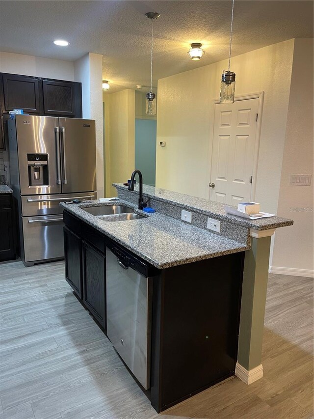 kitchen with an island with sink, light wood finished floors, appliances with stainless steel finishes, and a sink