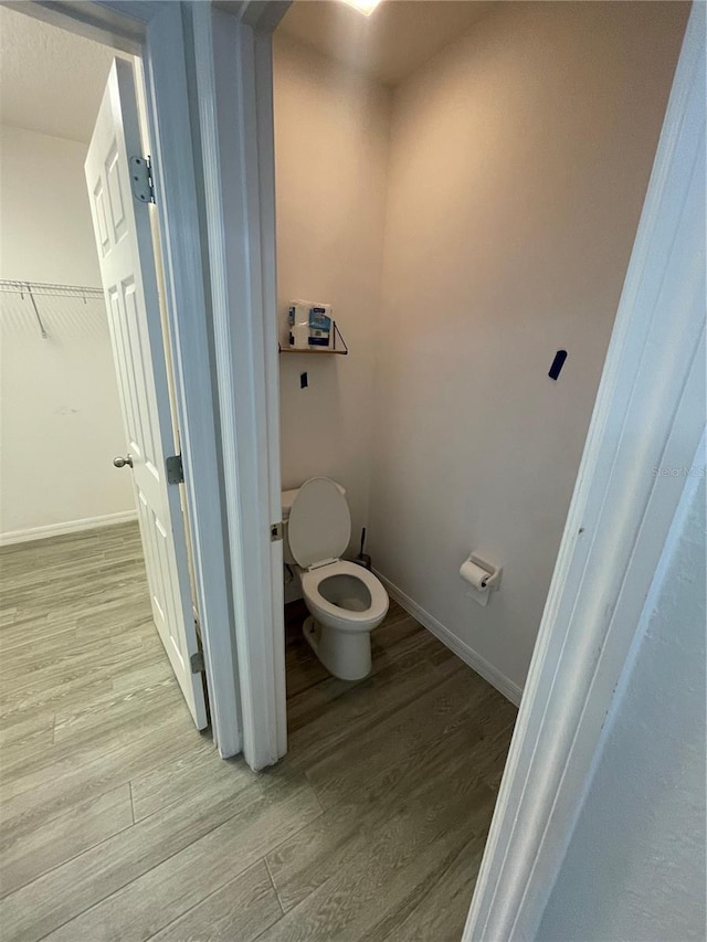 bathroom with toilet, baseboards, and wood finished floors