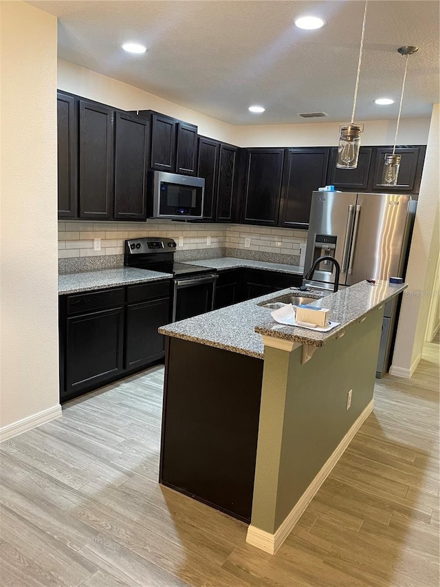 kitchen with appliances with stainless steel finishes, light wood-style floors, a sink, and dark cabinets