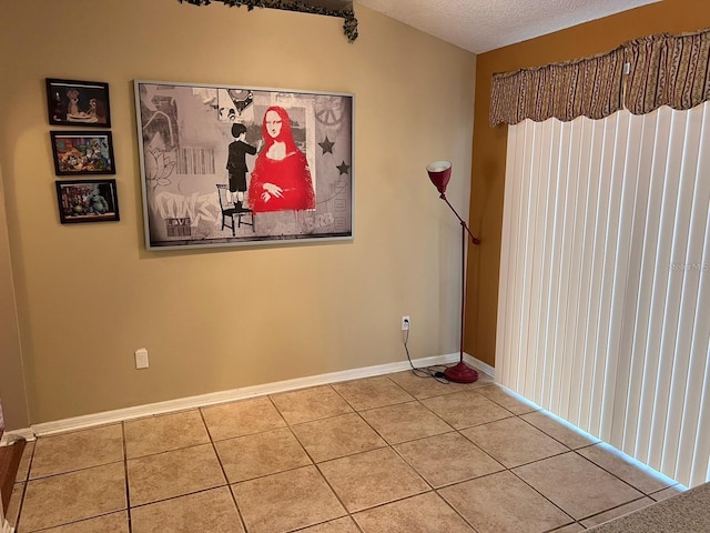 spare room featuring tile patterned floors, baseboards, a textured ceiling, and lofted ceiling