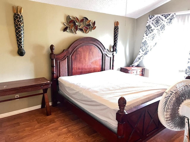 bedroom featuring vaulted ceiling, a textured ceiling, baseboards, and wood finished floors