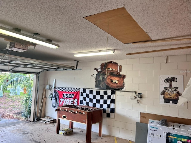 game room with concrete block wall, a textured ceiling, concrete floors, and a garage