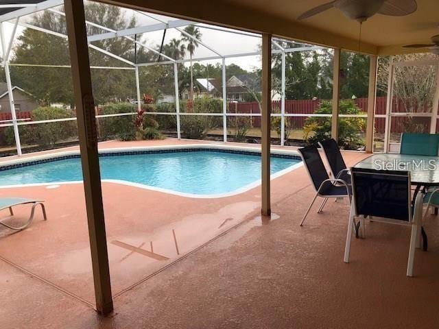 outdoor pool featuring glass enclosure, ceiling fan, a patio, and fence