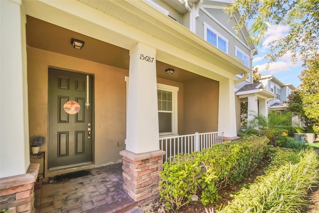 view of exterior entry featuring covered porch and stucco siding