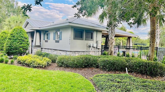 view of front of property featuring fence, stucco siding, a front lawn, stone siding, and metal roof