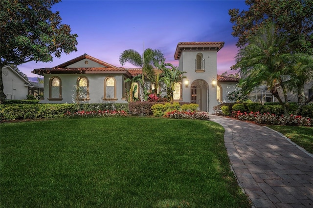 mediterranean / spanish-style house featuring a yard, a tiled roof, and stucco siding