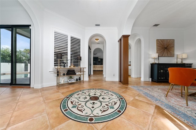 tiled entryway featuring arched walkways, visible vents, crown molding, and baseboards