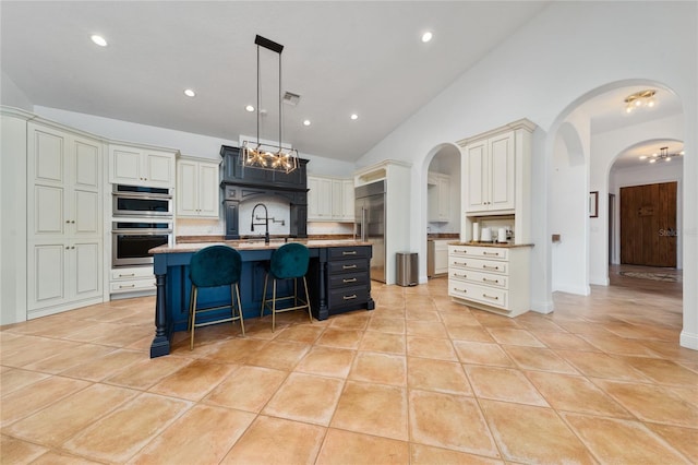 kitchen featuring arched walkways, light tile patterned flooring, stainless steel appliances, a sink, and a kitchen breakfast bar