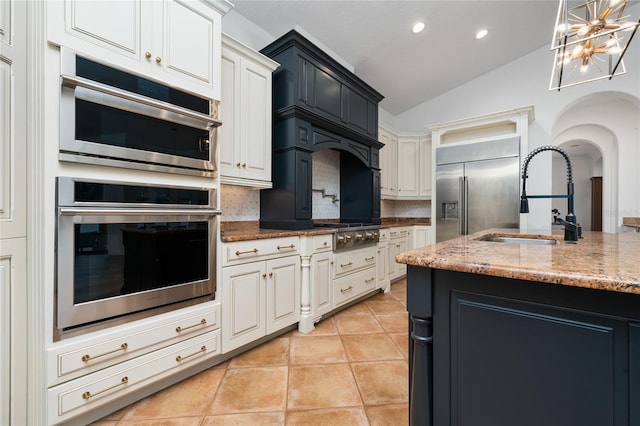 kitchen with tasteful backsplash, light stone counters, stainless steel appliances, a sink, and light tile patterned flooring