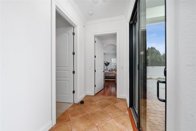 hallway featuring arched walkways, light tile patterned flooring, baseboards, and crown molding