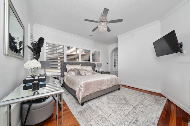 bedroom featuring baseboards, arched walkways, hardwood / wood-style floors, crown molding, and a textured ceiling