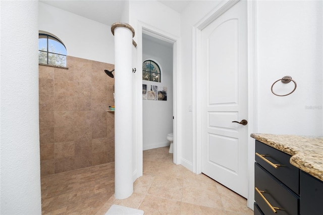 bathroom featuring baseboards, toilet, tile patterned floors, a tile shower, and vanity