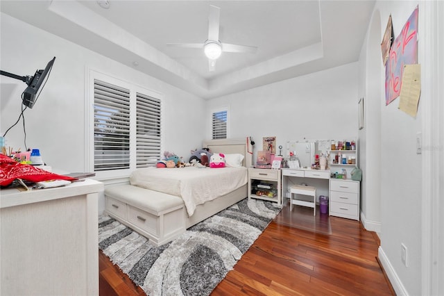 bedroom featuring a ceiling fan, a tray ceiling, baseboards, and wood finished floors