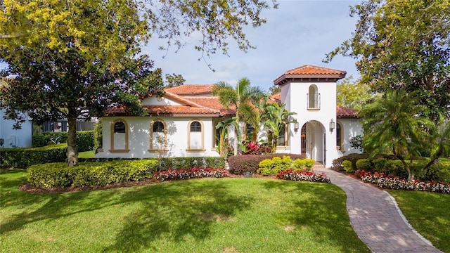 mediterranean / spanish home with a tile roof, a front lawn, and stucco siding