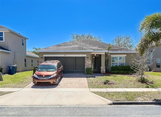 view of front of house with an attached garage, stone siding, decorative driveway, stucco siding, and a front yard