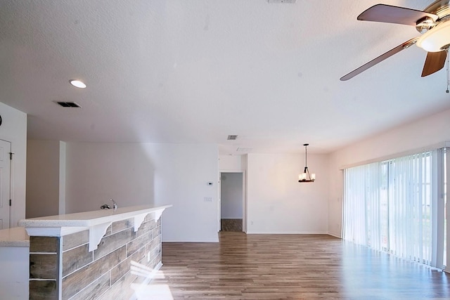 unfurnished living room featuring a ceiling fan, a textured ceiling, visible vents, and wood finished floors