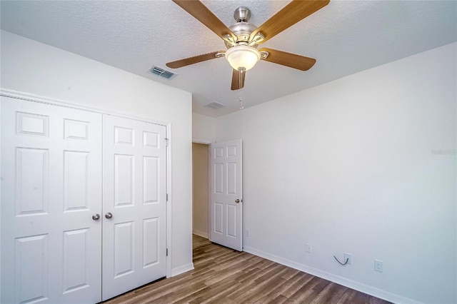 unfurnished bedroom with baseboards, visible vents, wood finished floors, a textured ceiling, and a closet