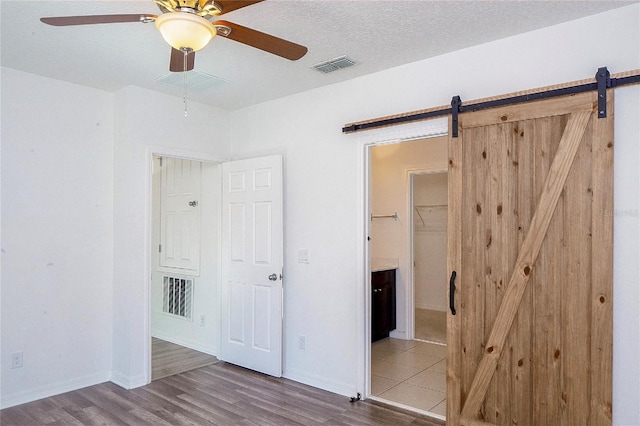 unfurnished bedroom featuring a barn door, visible vents, and wood finished floors