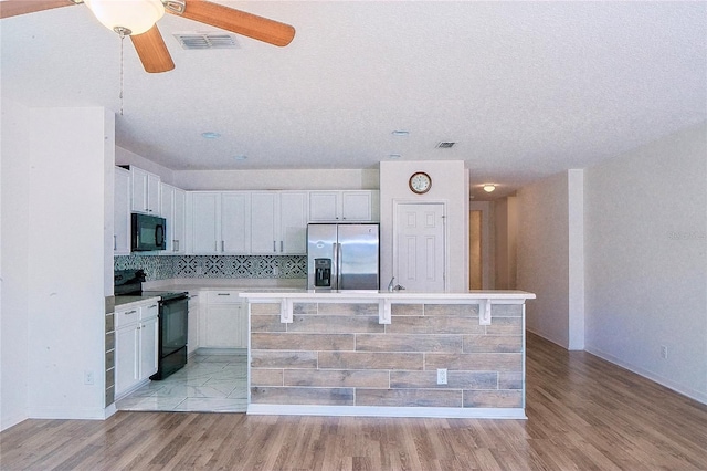 kitchen featuring white cabinetry, black appliances, light wood-style flooring, and visible vents