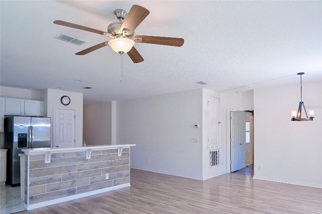 unfurnished living room with baseboards, visible vents, a textured ceiling, and light wood finished floors