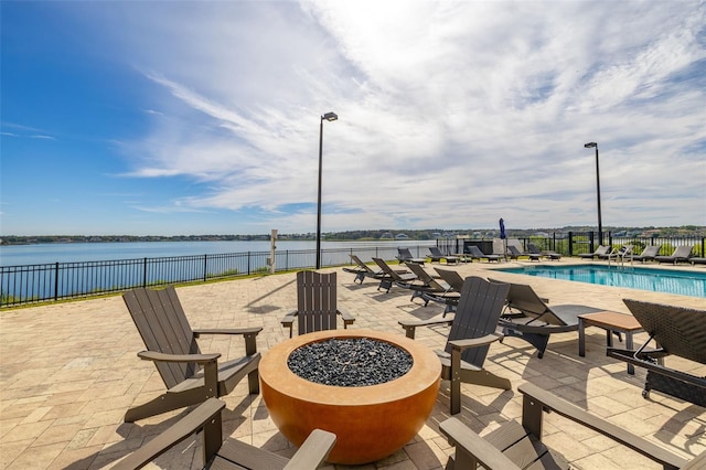 view of patio / terrace with a water view, an outdoor fire pit, a community pool, and fence