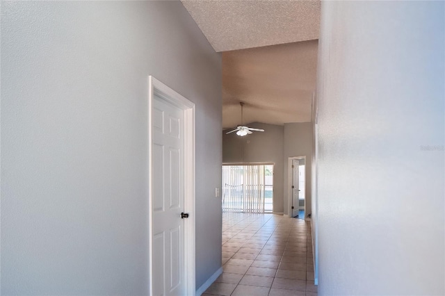 hallway with light tile patterned flooring, vaulted ceiling, a textured ceiling, and baseboards