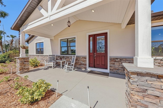 entrance to property featuring stone siding, covered porch, and stucco siding