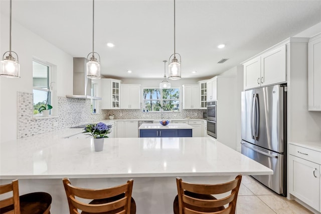 kitchen with wall chimney exhaust hood, tasteful backsplash, glass insert cabinets, and freestanding refrigerator