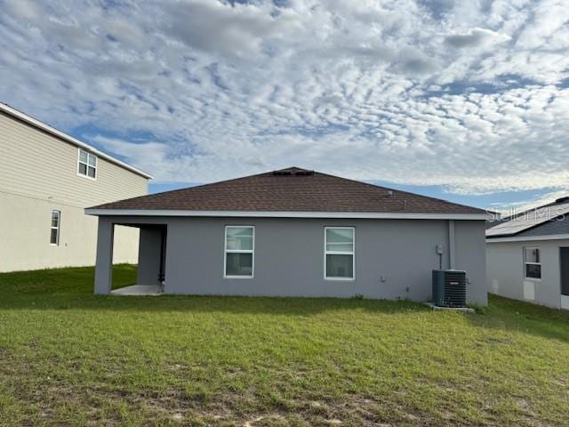 rear view of property featuring central air condition unit, a lawn, and stucco siding