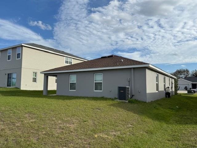 back of property featuring central AC unit, a lawn, and stucco siding