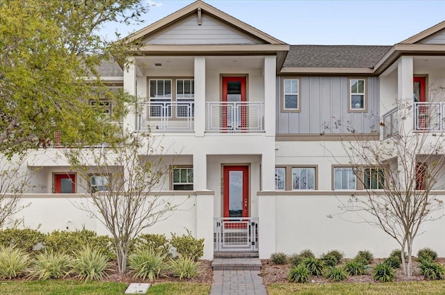 view of front of property featuring a balcony, a fenced front yard, a gate, board and batten siding, and stucco siding