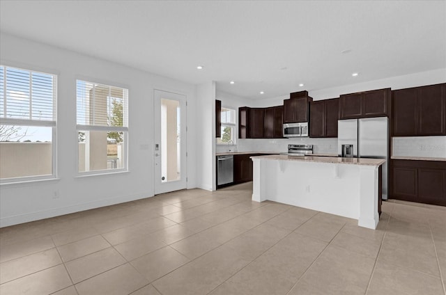 kitchen with light tile patterned floors, a kitchen island, appliances with stainless steel finishes, a kitchen breakfast bar, and dark brown cabinets