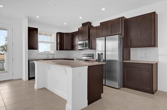 kitchen with light stone counters, dark brown cabinetry, stainless steel appliances, a kitchen island, and decorative backsplash