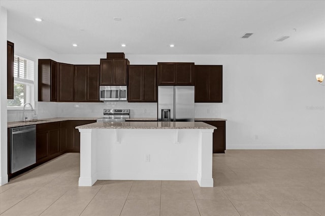 kitchen with stainless steel appliances, decorative backsplash, a sink, and a center island