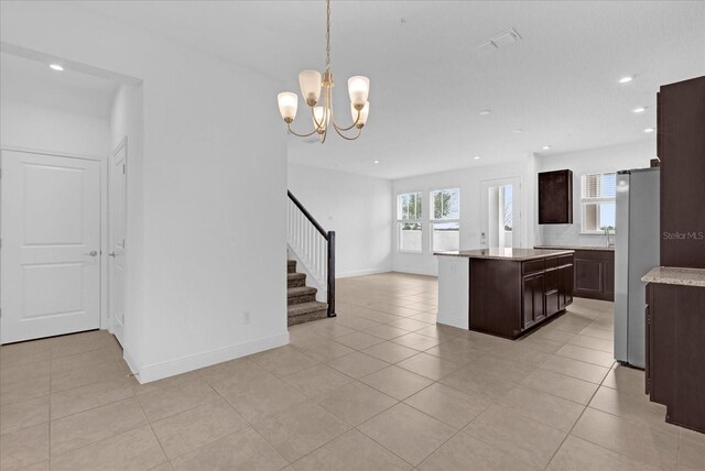 kitchen with a center island, freestanding refrigerator, light countertops, dark brown cabinets, and light tile patterned flooring