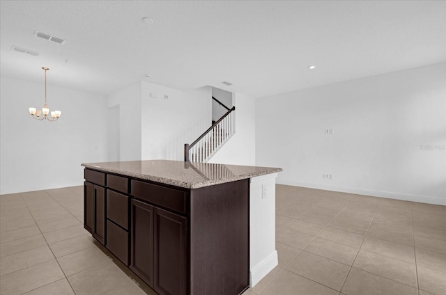 kitchen with light tile patterned flooring, a kitchen island, visible vents, and light stone countertops