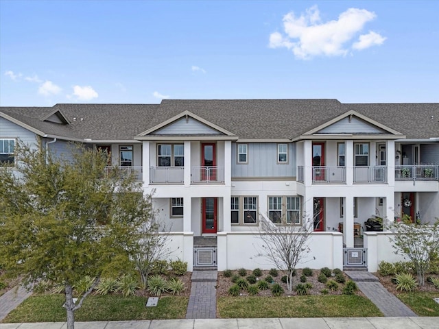 view of front facade with a shingled roof, a balcony, a fenced front yard, a gate, and board and batten siding