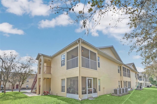 rear view of property featuring a yard, stucco siding, stairway, central AC unit, and a sunroom