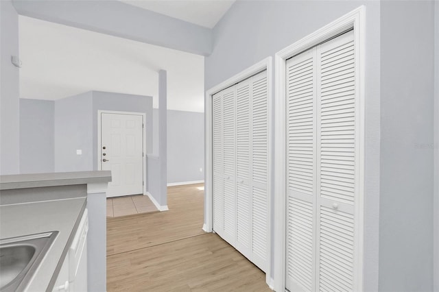 hallway featuring light wood-style floors, baseboards, and a sink