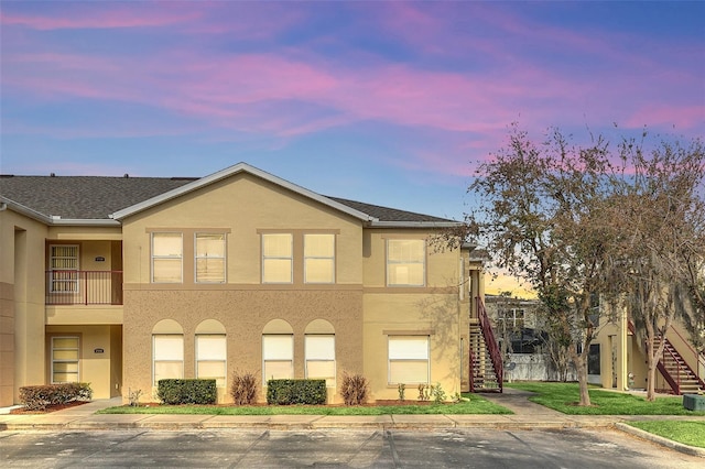 view of front facade with a yard, central AC unit, stairway, and stucco siding