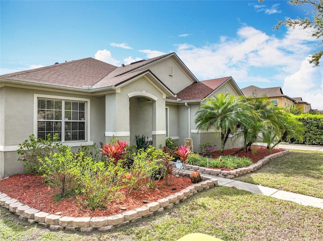 ranch-style house featuring a shingled roof, a front yard, and stucco siding