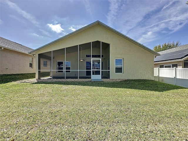 rear view of house with stucco siding, fence, a lawn, and a sunroom