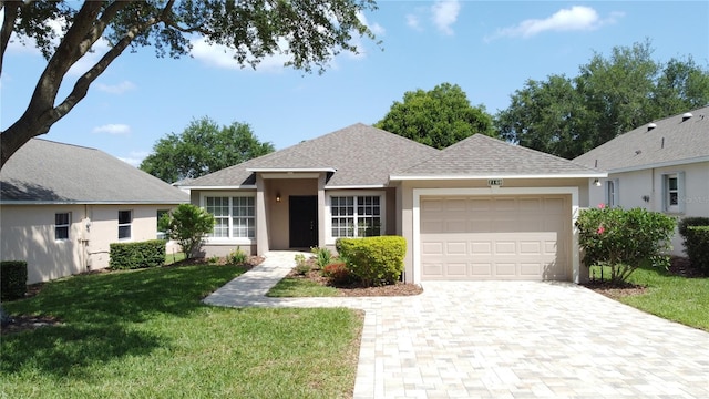 ranch-style house featuring an attached garage, a shingled roof, stucco siding, a front lawn, and decorative driveway