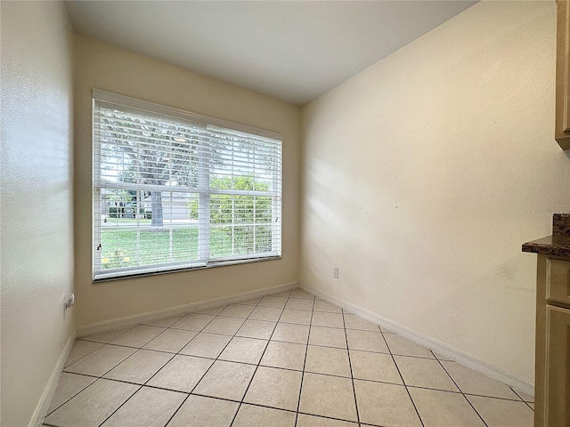 empty room featuring vaulted ceiling, light tile patterned floors, and baseboards