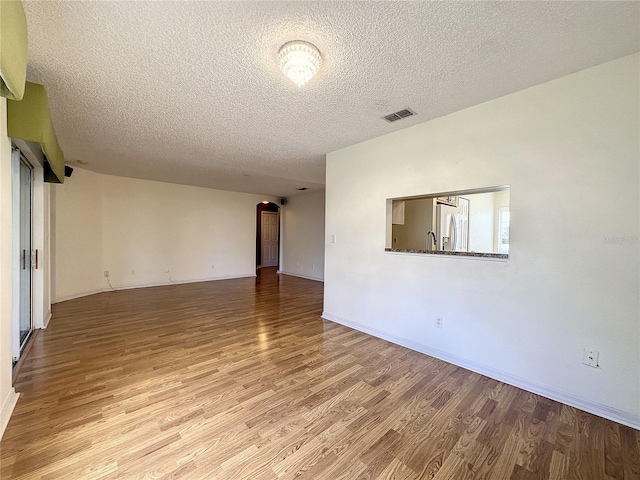 empty room with visible vents, a textured ceiling, baseboards, and wood finished floors