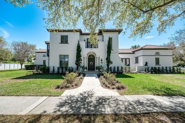 mediterranean / spanish home featuring a front lawn, a tiled roof, and fence