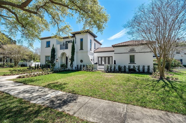 mediterranean / spanish-style house featuring stucco siding, a front lawn, a tile roof, fence, and a balcony